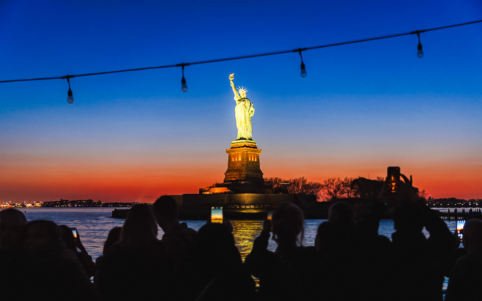 Statue of Liberty illuminated at night with sunset sky, viewed from a boat.