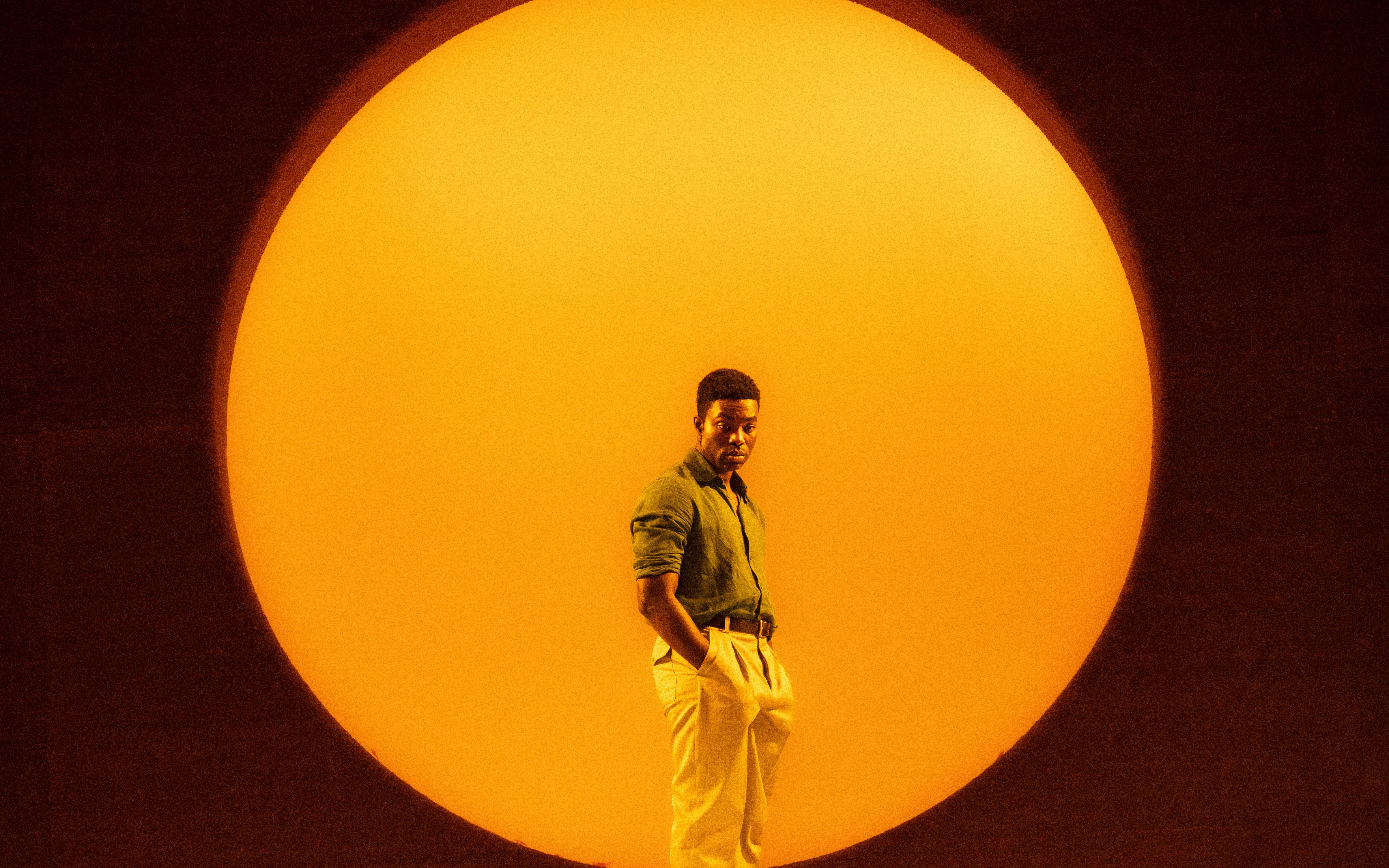Performer on stage with a large orange backdrop in All My Sons West End show.