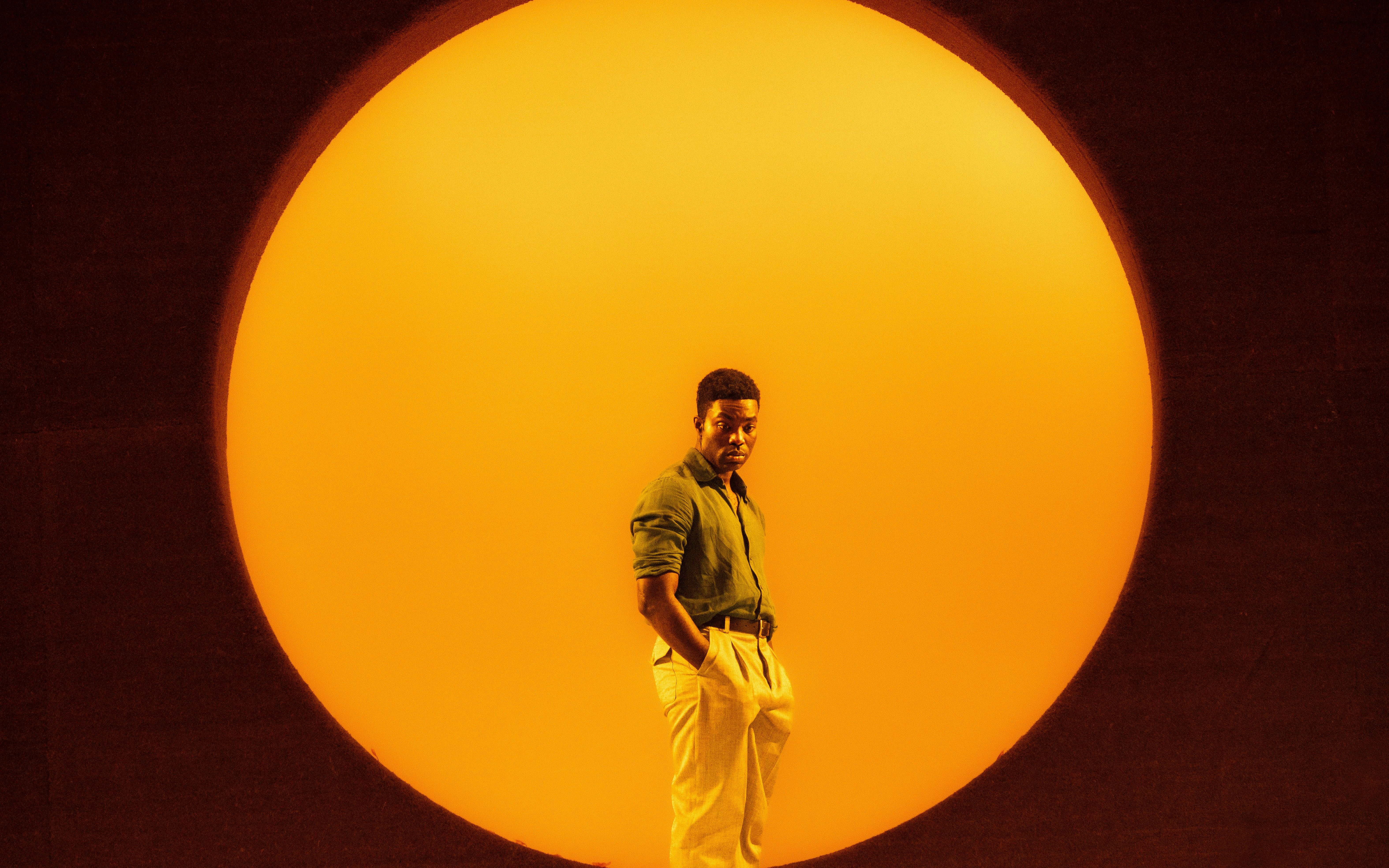 Performer on stage with a large orange backdrop in All My Sons West End show.