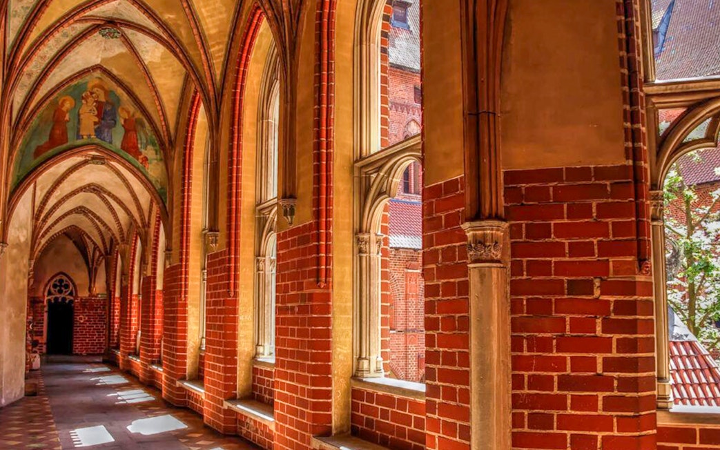 Gothic corridor inside Malbork Castle with arched windows and brick walls.