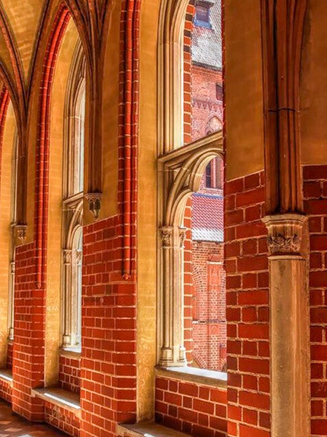 Gothic corridor inside Malbork Castle with arched windows and brick walls.