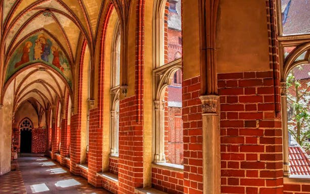 Gothic corridor inside Malbork Castle with arched windows and brick walls.