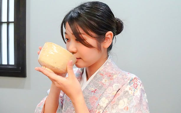 Woman in kimono sipping matcha from a traditional bowl in Japan.