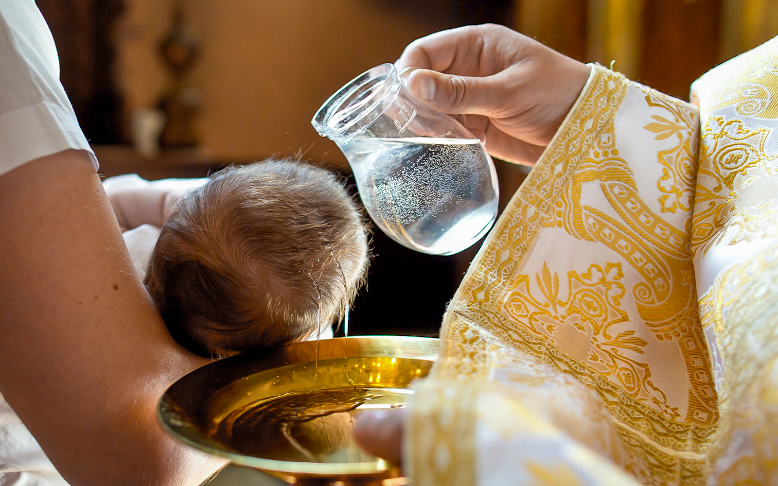 Baptism ceremony inside a church with priest and family gathered around the baptismal font.