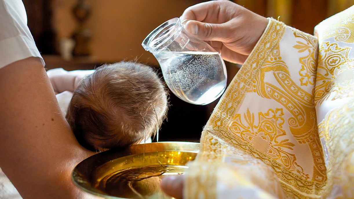 Baptism ceremony inside a church with priest and family gathered around the baptismal font.