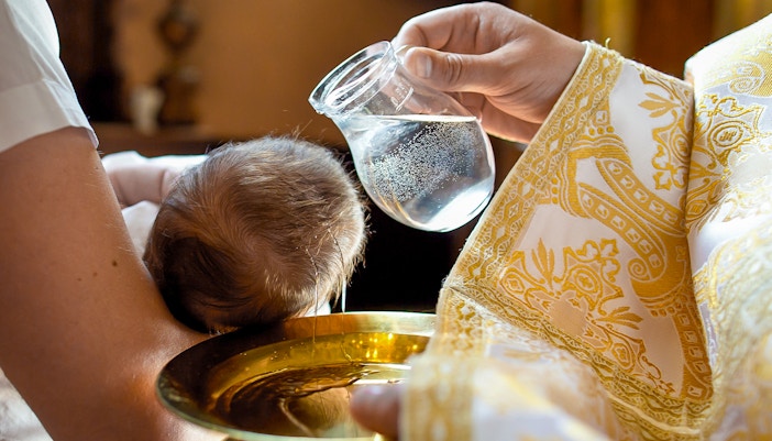 Baptism ceremony inside a church with priest and family gathered around the baptismal font.