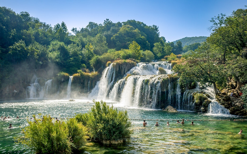 Waterfalls at Krka National Park with people swimming in the foreground.