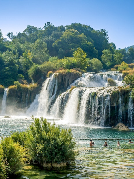 Waterfalls at Krka National Park with people swimming in the foreground.