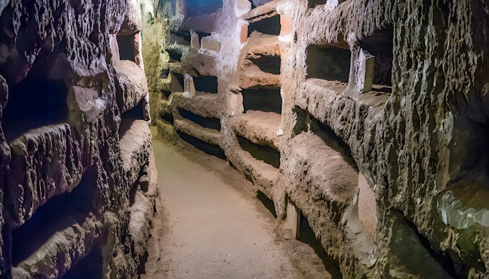 Tourists exploring ancient underground passages in the Catacombs of St. Callixtus, Rome.