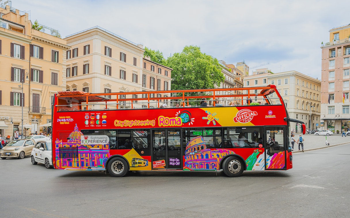 City Sightseeing bus in Rome with colorful graphics parked near historic buildings.