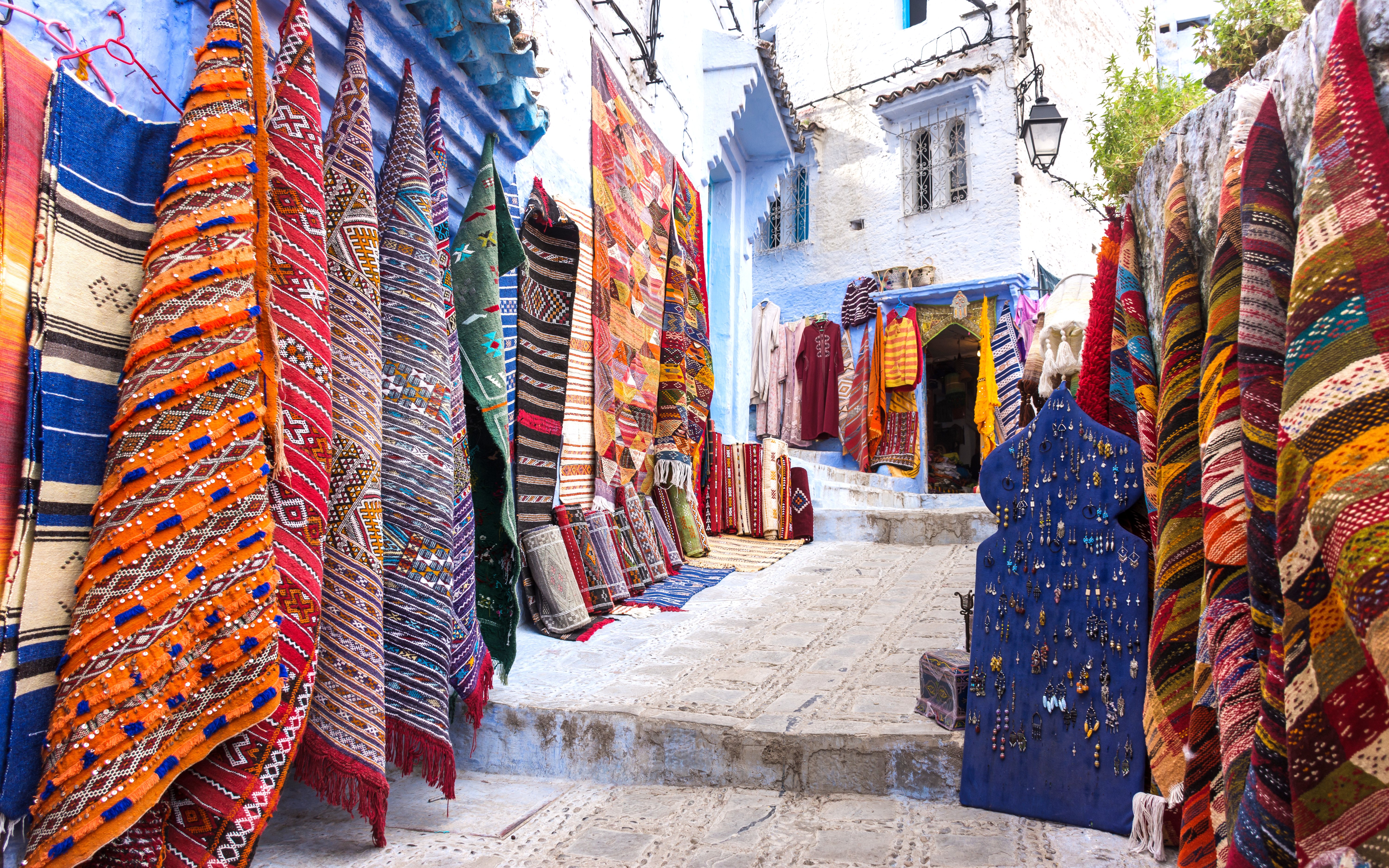 Colorful carpets displayed in a shop along a narrow street in Chefchaouen, Morocco.