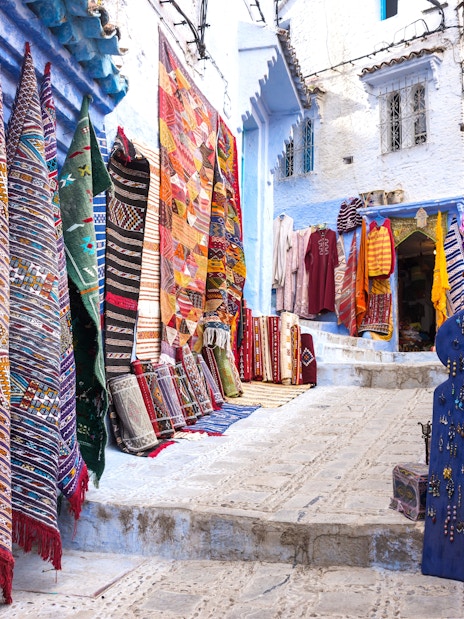 Colorful carpets displayed in a shop along a narrow street in Chefchaouen, Morocco.