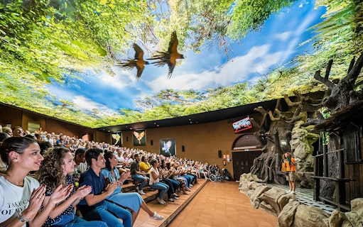 Audience watching a parrot show at Loro Park with a vibrant forest-themed ceiling.
