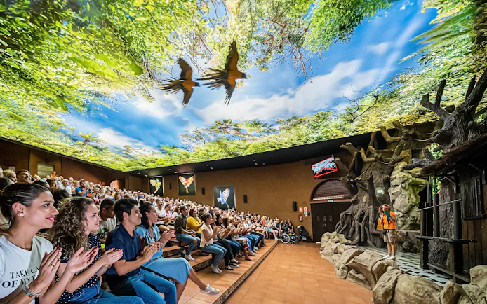 Audience watching a parrot show at Loro Park with a vibrant forest-themed ceiling.