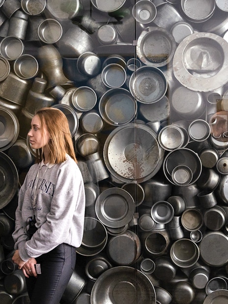 Enamelware display at Oskar Schindler's Factory, Krakow, with visitor observing.