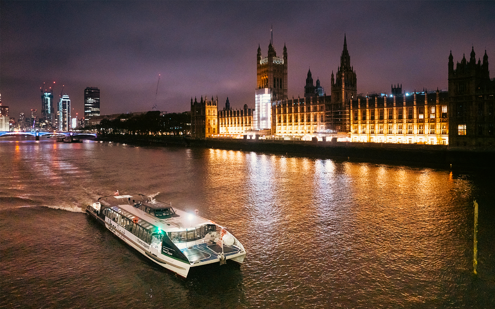 Uber Boat on Thames River at night passing illuminated Houses of Parliament, London.