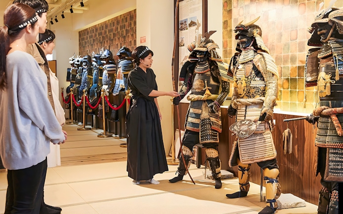Tour guide explaining samurai armor to visitors at Samurai Ninja Museum Tokyo.