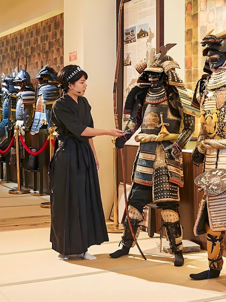 Tour guide explaining samurai armor to visitors at Samurai Ninja Museum Tokyo.