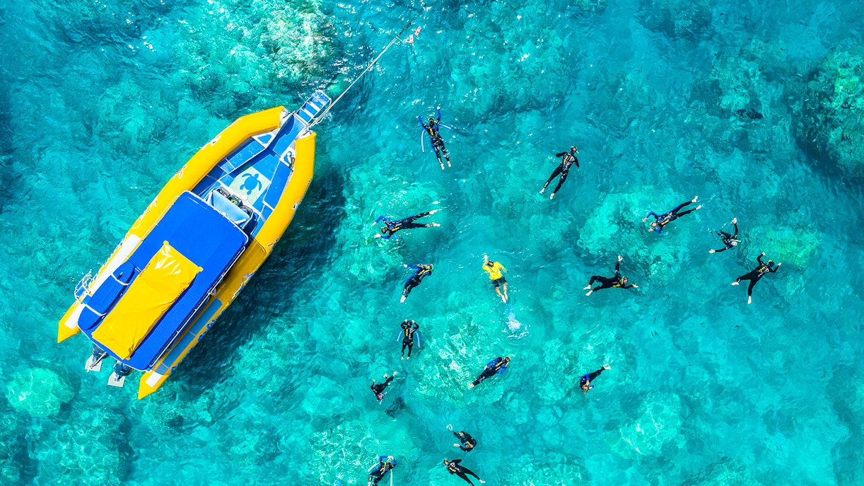Snorkelers near a yellow boat in clear waters of Whitsundays, Australia.