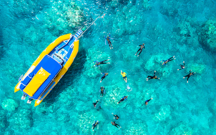 Snorkelers near a yellow boat in clear waters of Whitsundays, Australia.