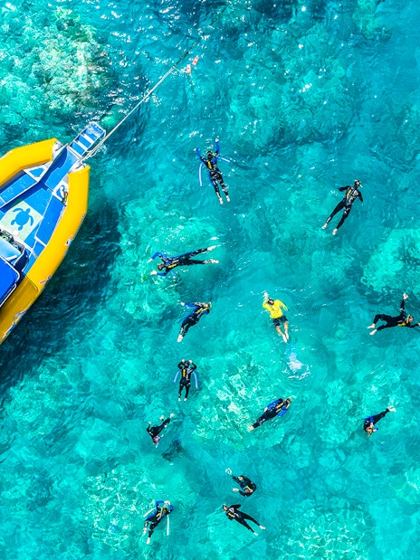 Snorkelers near a yellow boat in clear waters of Whitsundays, Australia.