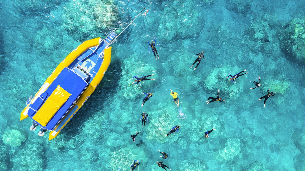 Snorkelers near a yellow boat in clear waters of Whitsundays, Australia.