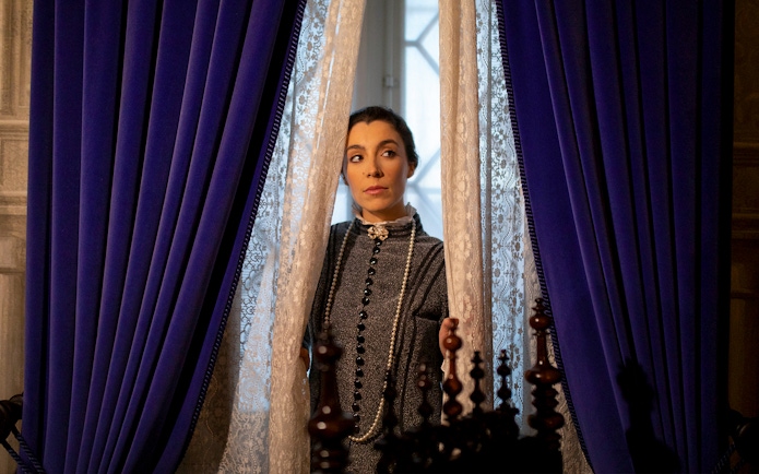Woman in period costume peering through lace curtains at the Palace of Pena, Portugal.