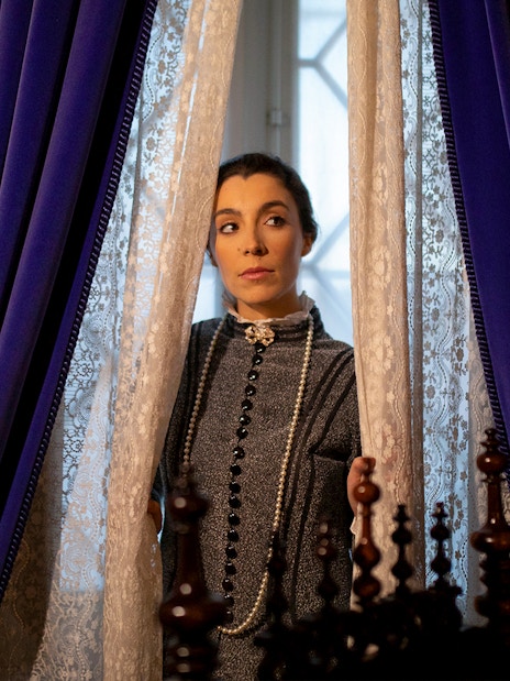 Woman in period costume peering through lace curtains at the Palace of Pena, Portugal.
