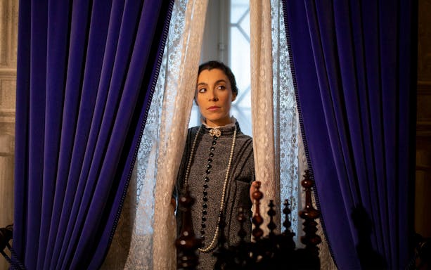 Woman in period costume peering through lace curtains at the Palace of Pena, Portugal.