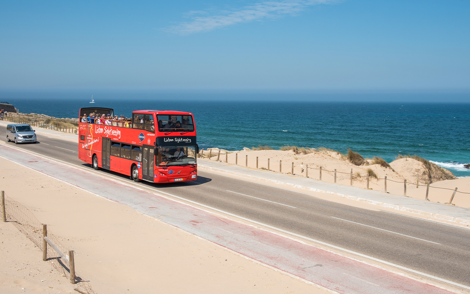 Lisbon Hop-On Hop-Off tour bus driving along oceanfront road.