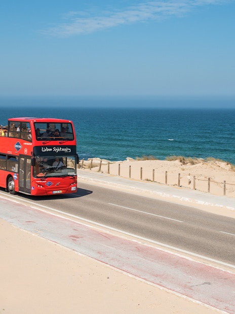 Lisbon Hop-On Hop-Off tour bus driving along oceanfront road.