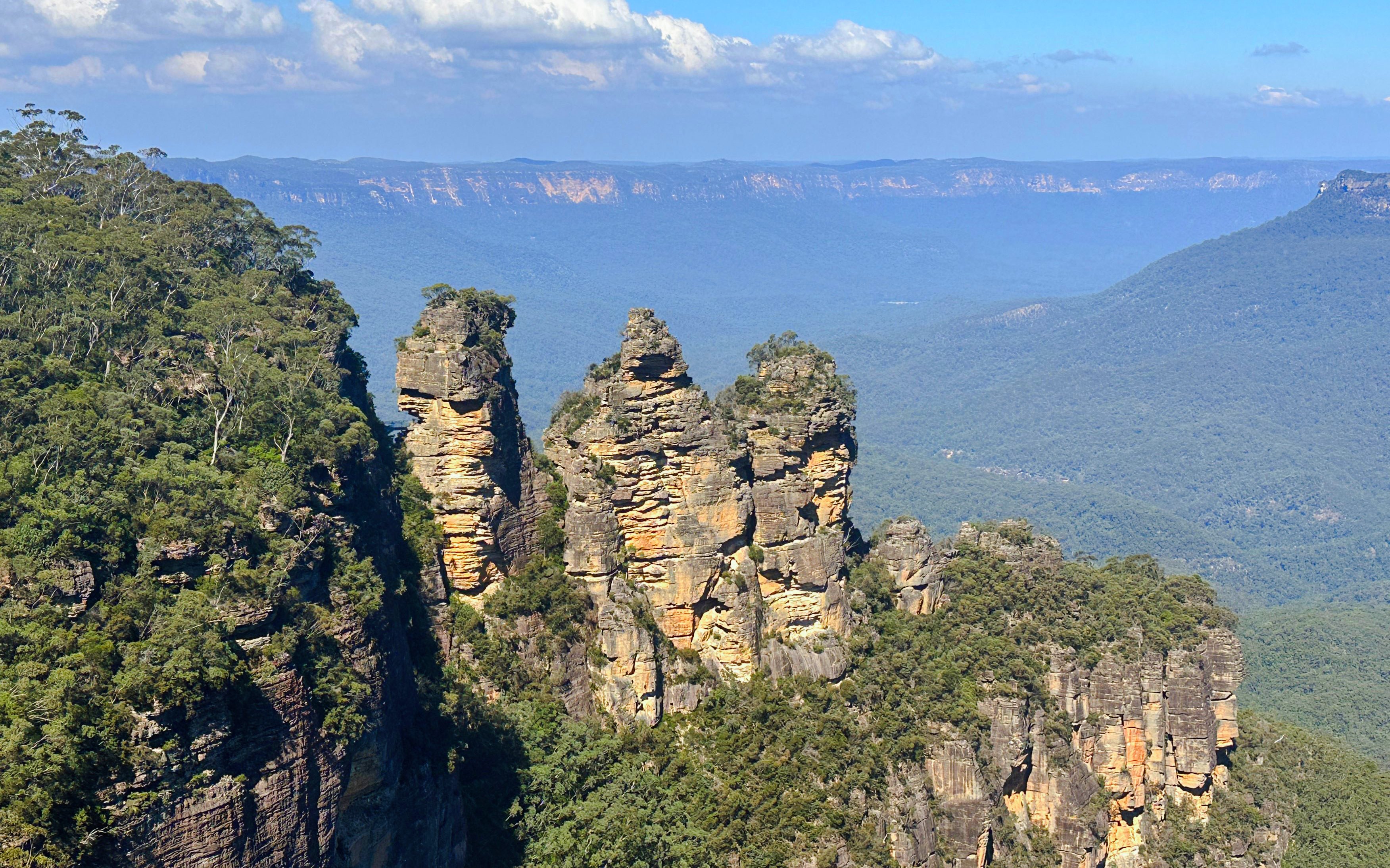 Three Sisters rock formation in Blue Mountains, Australia, with expansive forested landscape.