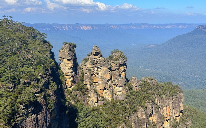 Three Sisters rock formation in Blue Mountains, Australia, with expansive forested landscape.