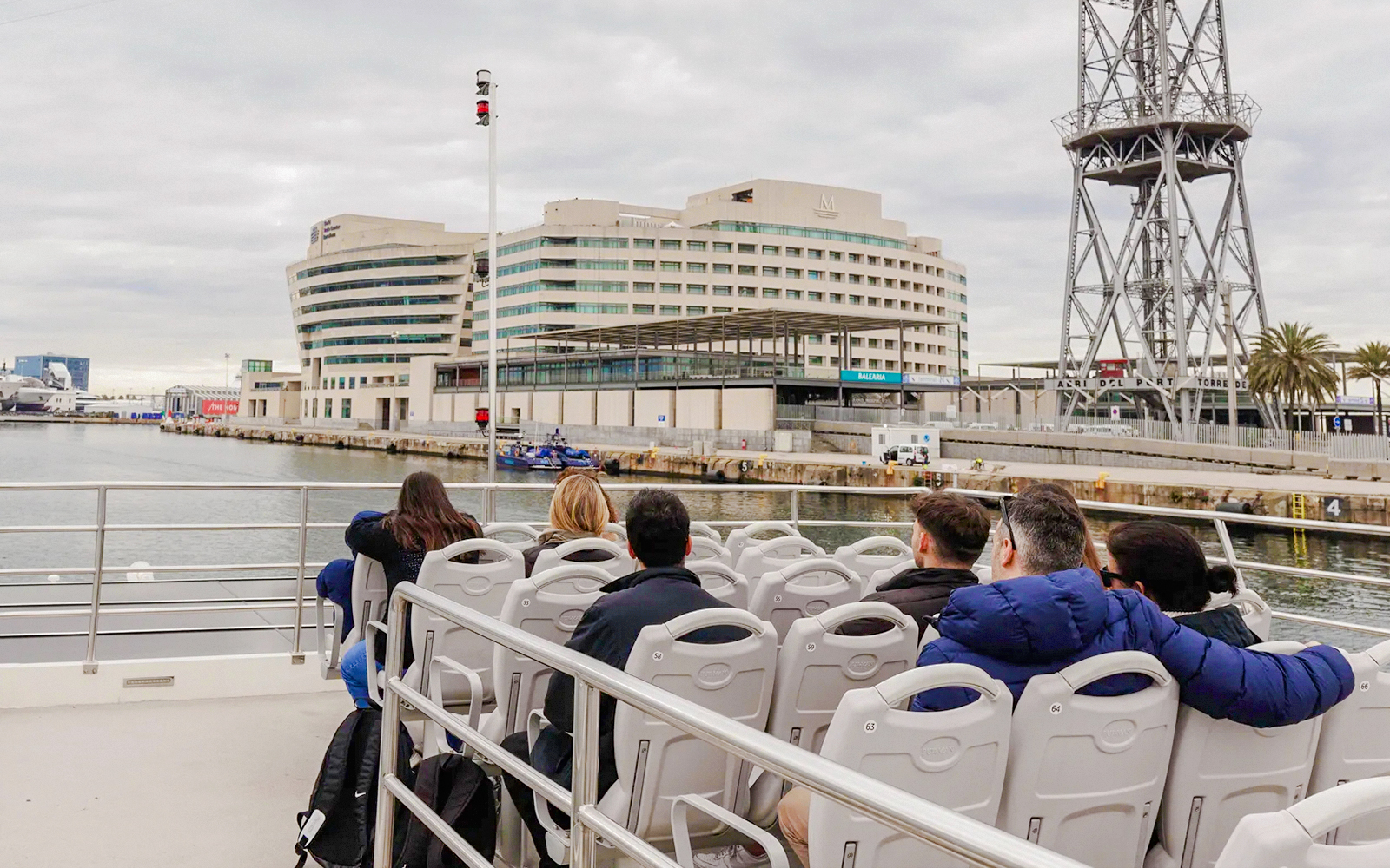 Tourists on a boat tour near a modern building and tower in a harbor.