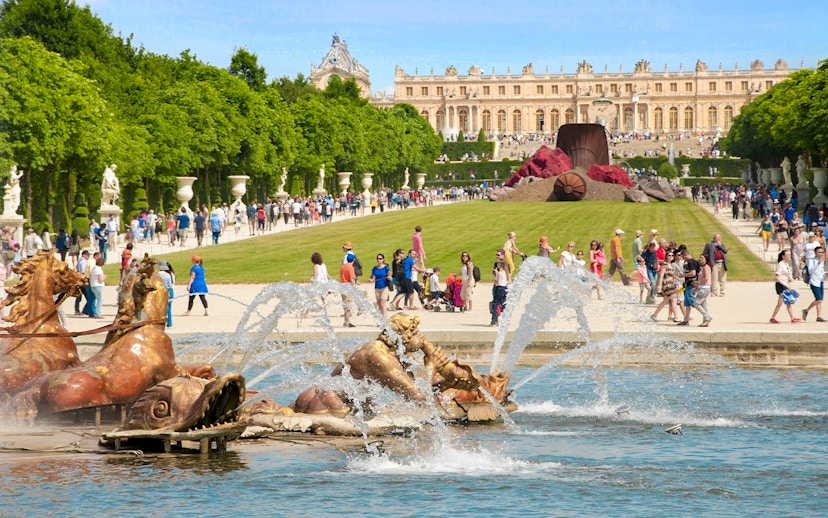Musical fountain at the Palace of Versailles with sculptures and visitors in the background.