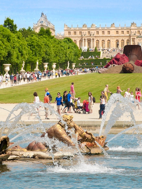 Musical fountain at the Palace of Versailles with sculptures and visitors in the background.