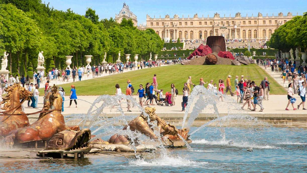Musical fountain at the Palace of Versailles with sculptures and visitors in the background.