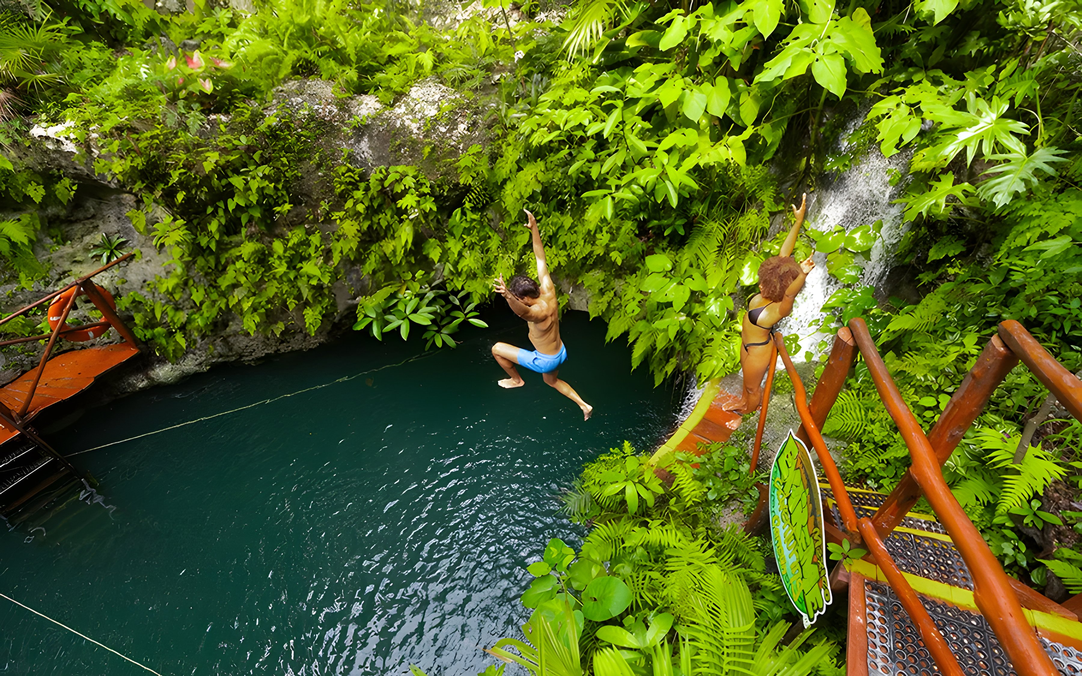Couple enjoying a jump into a lush cenote surrounded by greenery.