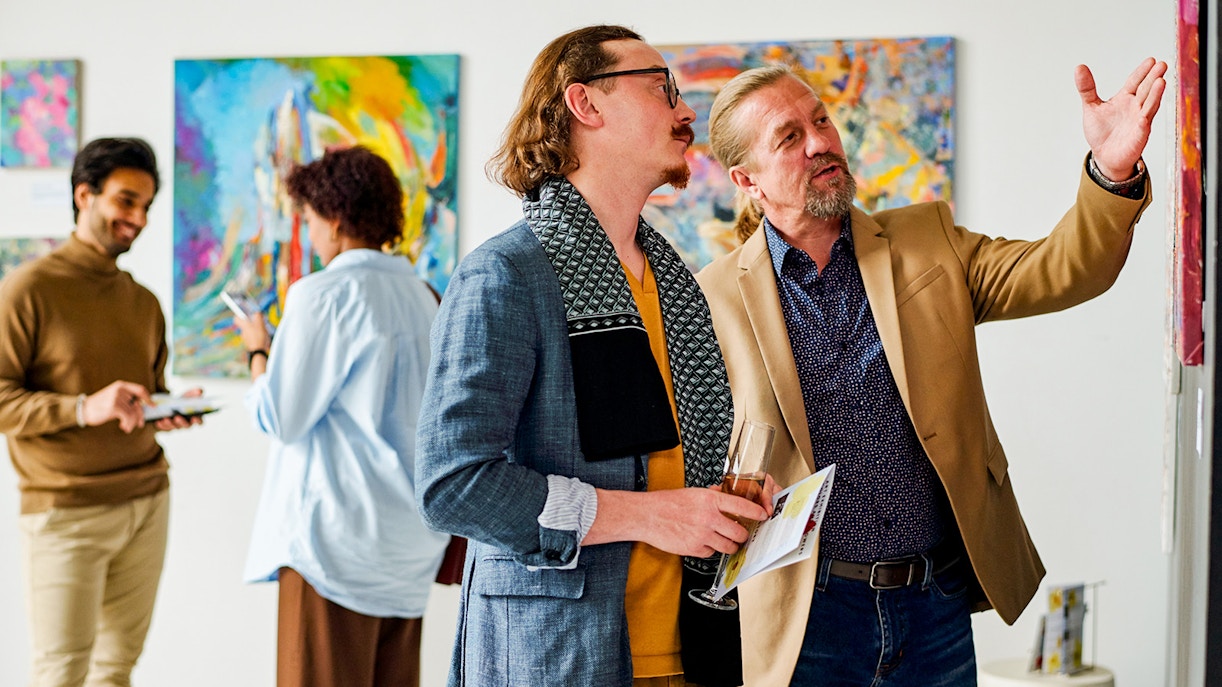 Art enthusiasts engaged in a lively discussion at an exhibition, with vibrant paintings in the background, capturing the interactive spirit of Uffizi Gallery events
