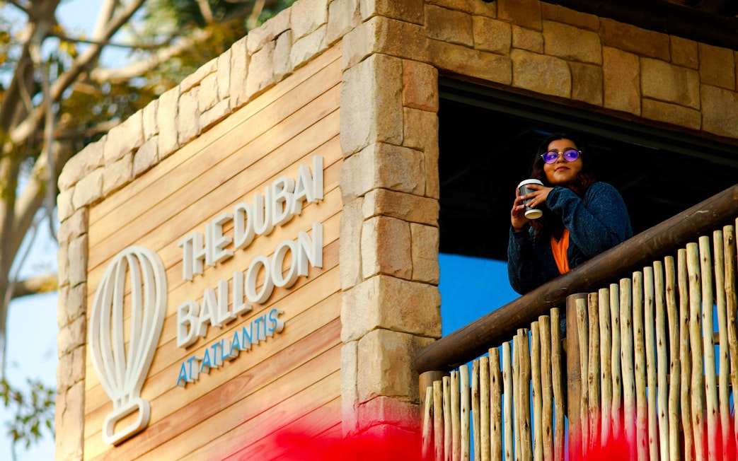 The Dubai Balloon sign at Atlantis with a person enjoying a drink on the balcony.