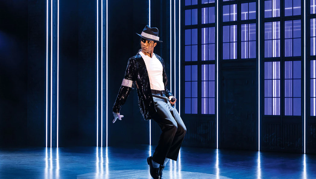 Performer in MJ Das Musical dancing on stage with blue-lit backdrop.