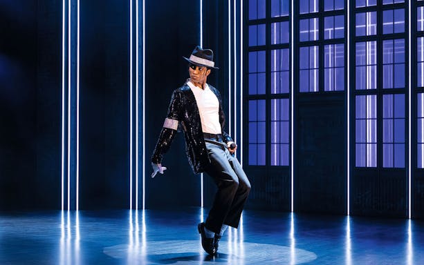 Performer in MJ Das Musical dancing on stage with blue-lit backdrop.