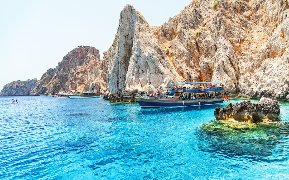 Boat near rocky cliffs on Suluada Island, Antalya, with tourists enjoying the view.