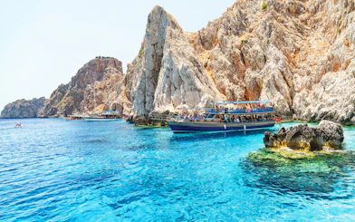 Boat near rocky cliffs on Suluada Island, Antalya, with tourists enjoying the view.