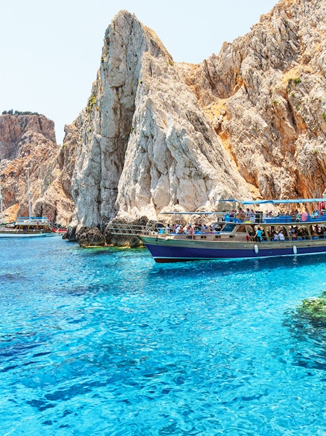 Boat near rocky cliffs on Suluada Island, Antalya, with tourists enjoying the view.