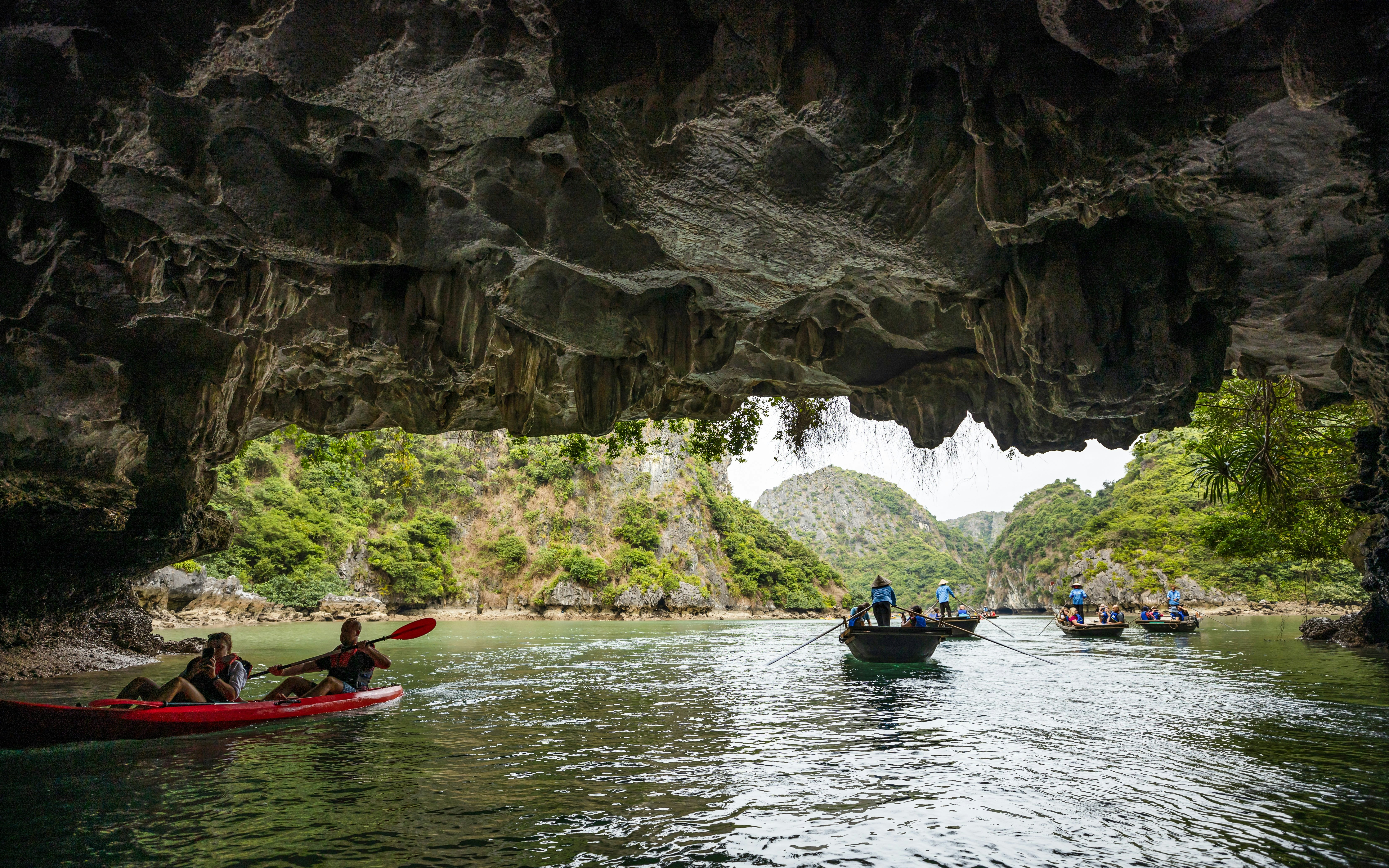Kayakers and rowboats inside Luon Cave, Halong Bay, Vietnam, surrounded by limestone formations.