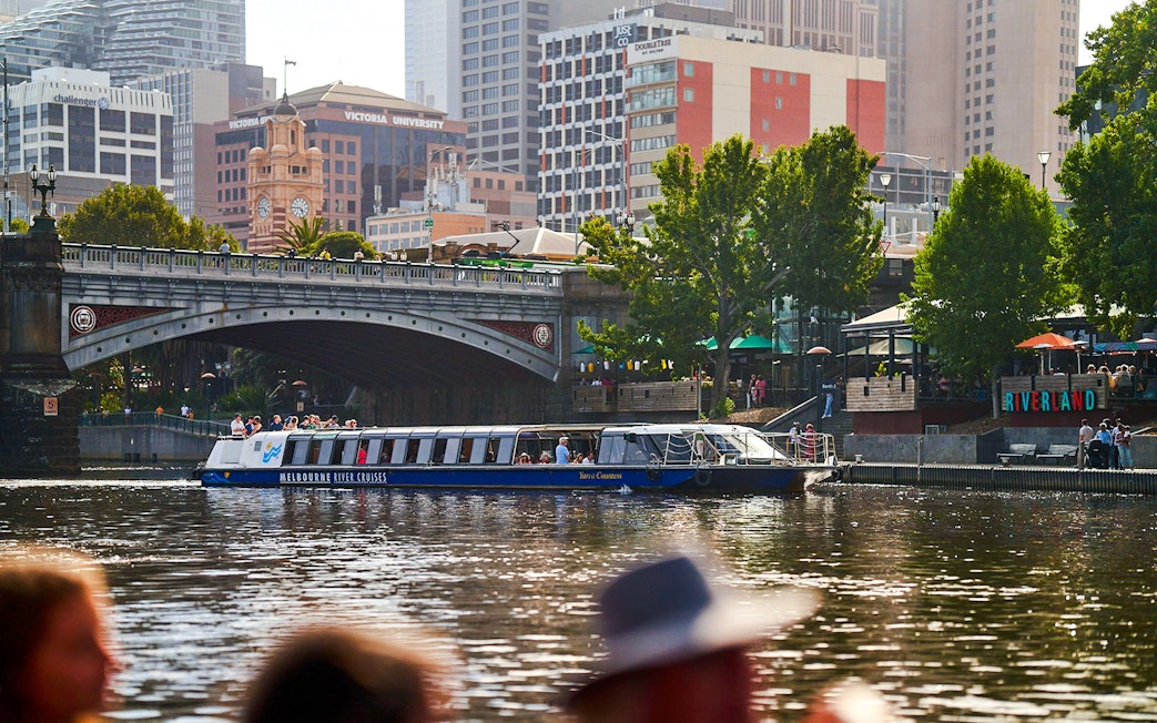 Melbourne River Cruises boat on Yarra River with city skyline and bridge in background.