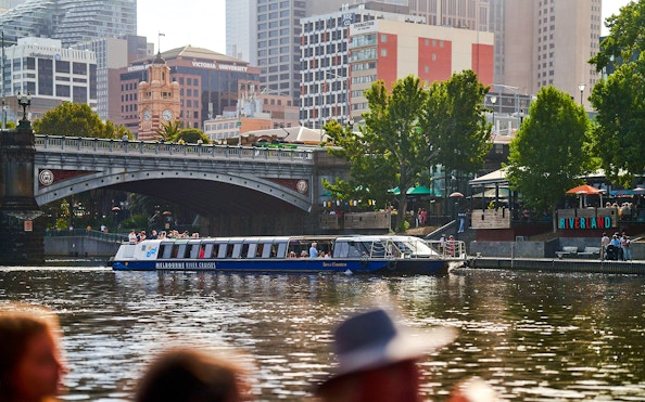 Melbourne River Cruises boat on Yarra River with city skyline and bridge in background.