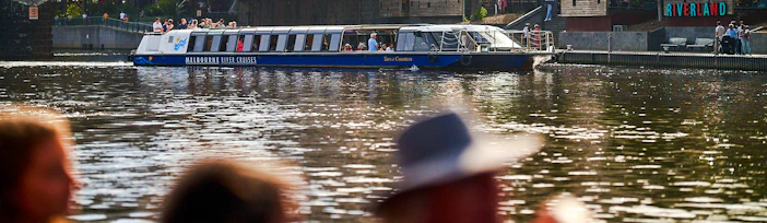 Melbourne River Cruises boat on Yarra River with city skyline and bridge in background.