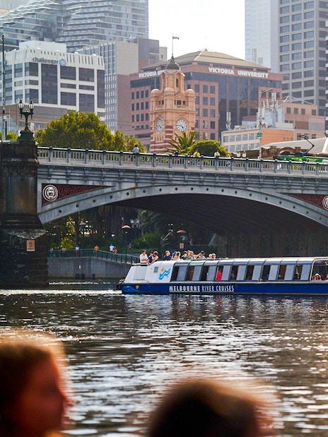 Melbourne River Cruises boat on Yarra River with city skyline and bridge in background.